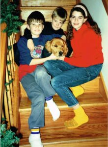 two boys and a girl sit on stairs with a golden retreiver